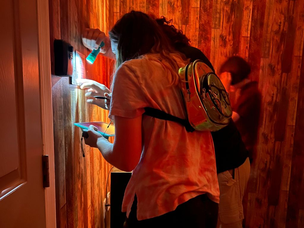 Family working together to solve a glowing puzzle clue inside a themed escape room at Worlds Away Escape in Winchester, Virginia